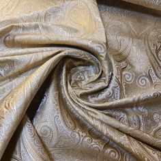 a close up view of a gold fabric with white paisley designs on it's side