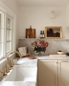 a white kitchen with marble counter tops and gold faucet, an open window over the sink