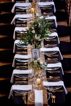 the table is set with black and white linens, gold place settings, and greenery