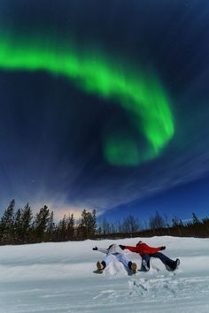 two people laying in the snow under an aurora bore