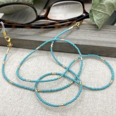 Simple and bohemian eyeglasses necklace made with Preciosa Czech crystal seed beads in Turquoise tones with tiny gold plated crystal seed beads.  Paired with delicate gold plated crystal seed beads , this handmade eyeglass chain will definitely create a unique look. This eyeglass lanyard is made on strong quality beading wire with gold plated wire guardians that protect the quality white eyeglass holder grips. The necklace is ended with spring clasps that hold the eyeglass grips and they can be Blue Glasses Chains With Colorful Beads For Beach, Glass Bead Necklaces For Beach, Glass Necklaces With Tiny Beads For The Beach, Glass Tiny Beads Necklace For Beach, Blue Beaded Glasses Chain For Beach, Bohemian Glasses Chains With Tiny Beads For Beach, Adjustable Glass Beaded Necklaces With Tiny Beads, Adjustable Blue Glasses Chains With Colorful Beads, Adjustable Glass Beaded Necklace With Tiny Beads