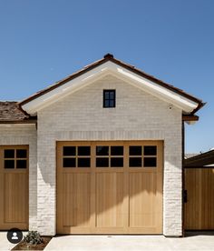 a white brick house with two brown garage doors