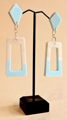 a pair of white and blue square shaped earrings on a black stand with a beige background