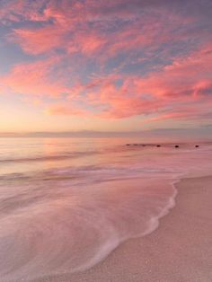 the sun is setting at the beach with waves coming in to shore and pink clouds