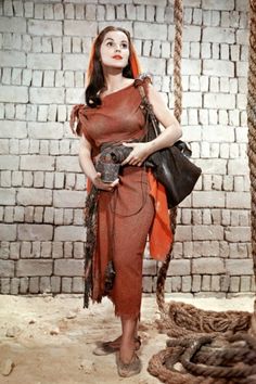 a woman standing in front of a brick wall holding a black purse and wearing an orange dress