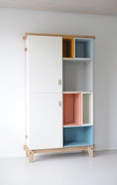 a white cabinet with multicolored shelves in an empty room next to a wall