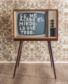 an old tv sitting on top of a wooden tripod in front of a wall