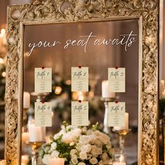 a table with candles, flowers and seating cards on it in front of a mirror