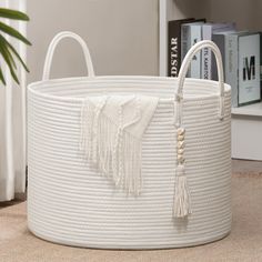 a large white basket with tassels on the handle and handles is sitting in front of a book shelf