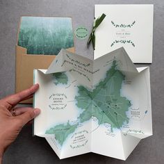 a hand is holding an open book with maps on it and green ribbon around the pages