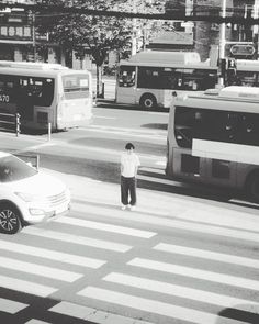 a man standing in the middle of a crosswalk with buses and cars behind him