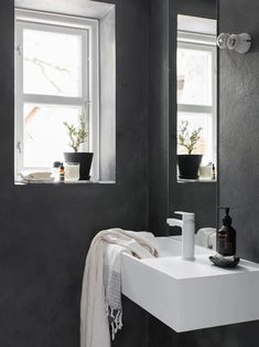 a white sink sitting under a bathroom mirror next to a window with potted plants