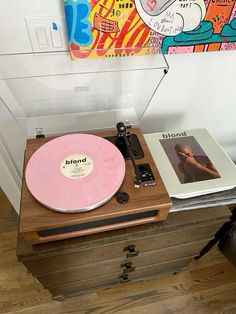 an old record player sitting on top of a wooden table next to a wall painting