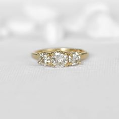 three stone diamond ring in yellow gold setting on white background with soft light from behind