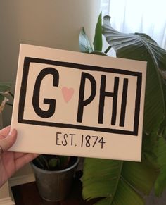 a person holding up a sign with the word g p h on it in front of a potted plant