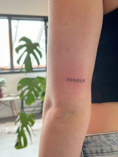 a woman's arm with the word sonder tattooed on her left arm, next to a potted plant