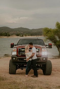 a man and woman standing in front of a truck with the hood up, kissing