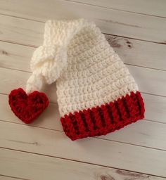 a white and red knitted hat with a heart on the side sitting on a wooden floor