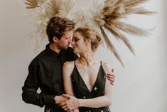 a man and woman standing next to each other in front of a wall with feathers on it