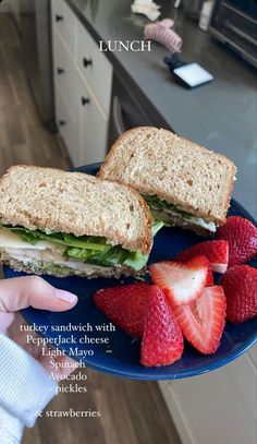 someone holding a plate with a sandwich and strawberries on it