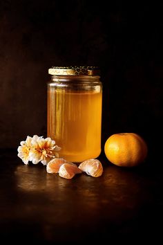 a jar of honey next to an orange and some flowers on a dark table with a black background