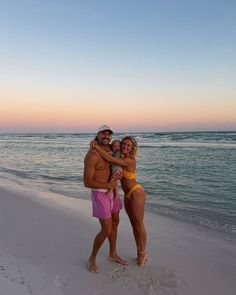 a man and woman standing on the beach at sunset with their arms around each other