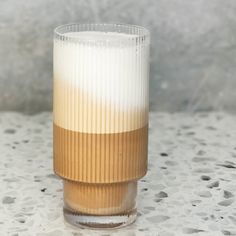 a tall glass sitting on top of a white table next to a brown and white cup