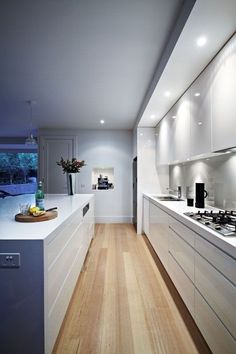 a modern kitchen with white cabinets and wood flooring is lit by recessed lighting