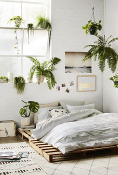 a bed with white sheets and pillows in a room filled with potted plants on the wall