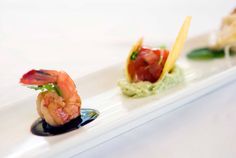 three small appetizers on a white plate with sauce and garnishes