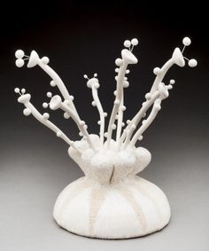 a white vase with many branches and balls on it's top, in front of a black background