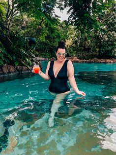 a woman standing in the water holding a drink with her right hand and wearing goggles