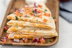 quesadillas stacked on a wooden tray with onions and tomatoes, garnished with cilantro