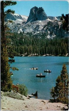 there are many boats on the water in this lake with mountains in the back ground