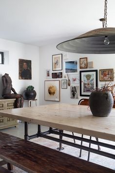 a wooden table sitting in the middle of a room with pictures on the wall behind it