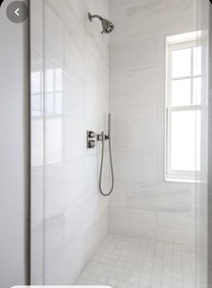 a white tiled bathroom with a shower head and hand held shower faucet in the corner