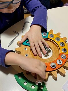 a young child is playing with a wooden toy that looks like a gear wheel and has buttons on it