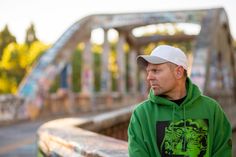 a man in a green hoodie and white cap standing on a bridge looking off into the distance