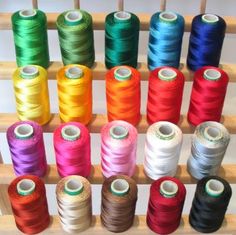 many spools of thread are lined up on a wooden rack in front of each other