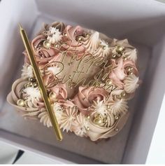 a birthday cake in a box with a pen on the top and flowers around it