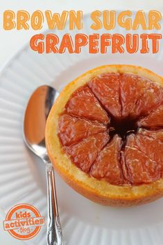 a grapefruit cut in half on a white plate with spoons and fork