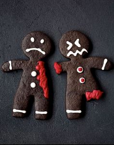 two decorated gingerbread men on a black surface with red and white icing around them