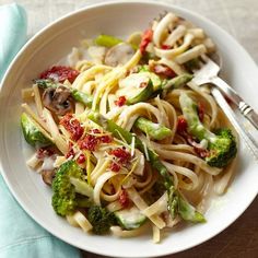 a white bowl filled with pasta and broccoli on top of a wooden table