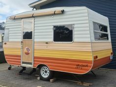 an orange, yellow and white trailer parked in front of a blue building with windows