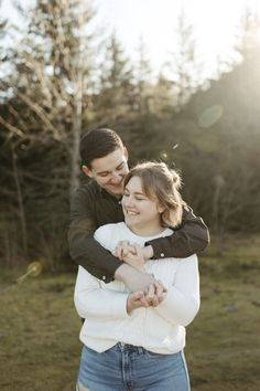 a man holding a woman in his arms and smiling at the camera with trees in the background