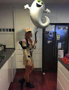 a woman is holding an inflatable balloon while standing next to a refrigerator and cabinets