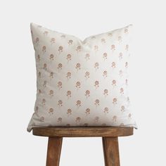 a white pillow with brown flowers on it sitting on top of a wooden stool in front of a wall