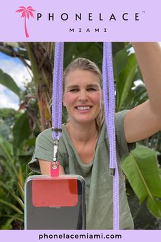 a woman is smiling while hanging on a rope in front of some trees and plants