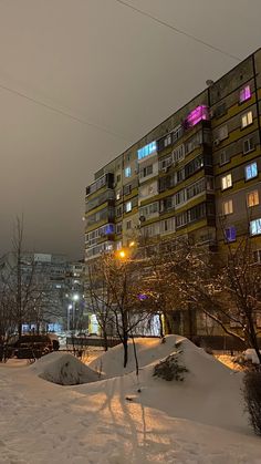 an apartment building is lit up at night in the snow covered area next to trees