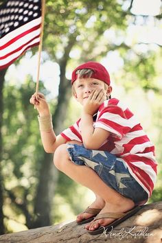 a young boy sitting on top of a tree trunk holding an american flag